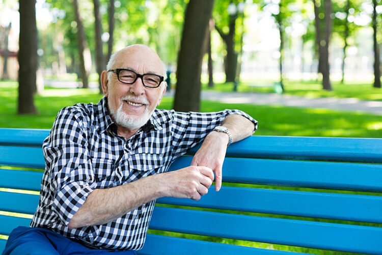 Senior entspannt Älterer Mann lehnt sich locker an die Lehne einer Parkbank.
