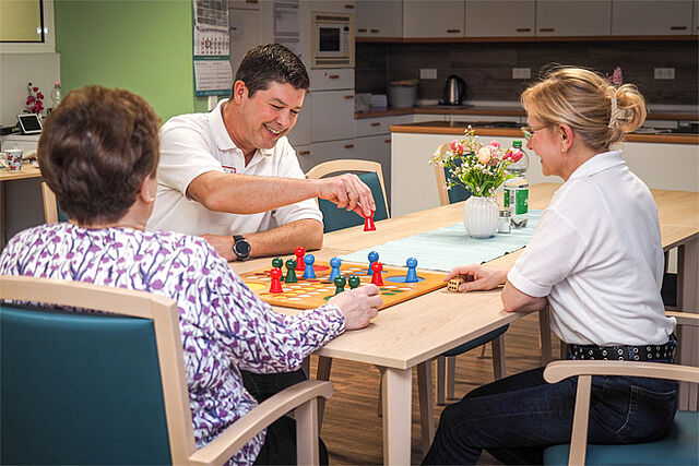 Tagespflege Zwei Pflegekräfte spielen mit einer Seniorin "Mensch ärgere Dich nicht".
