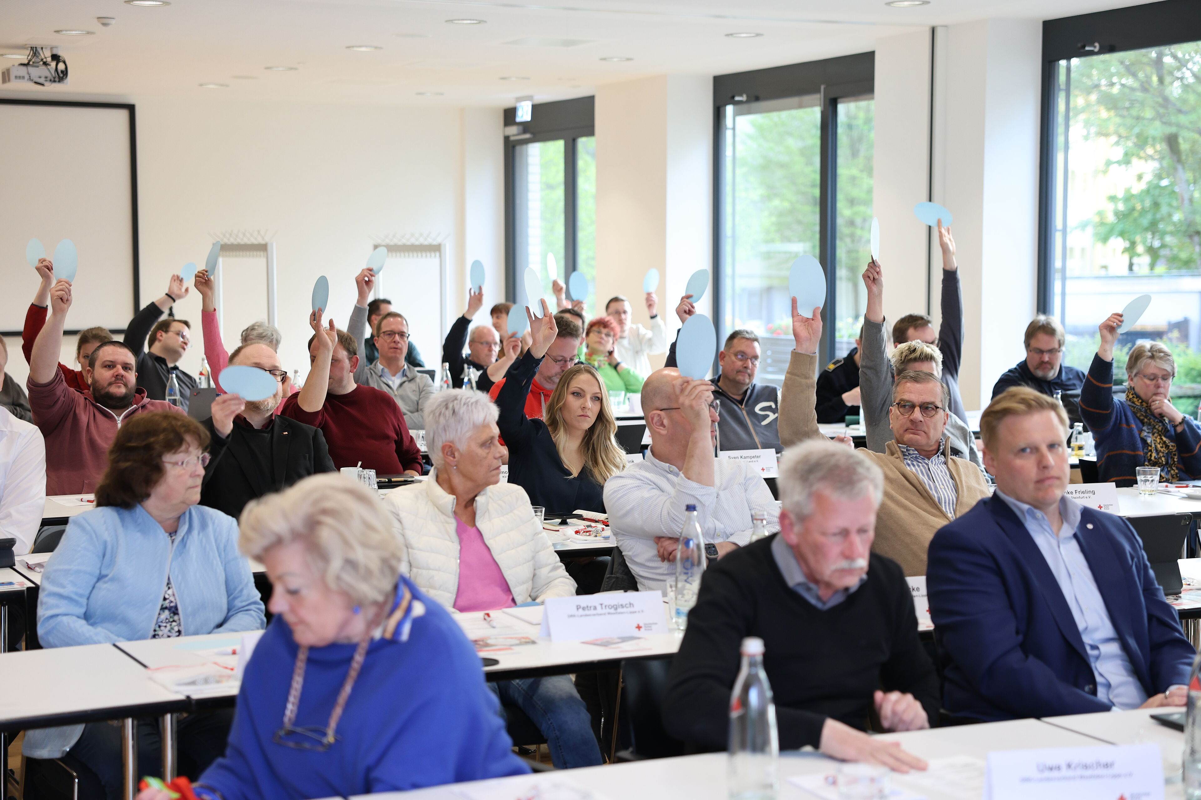 Menschen an Tischreihen stimmen per Handzeichen ab.