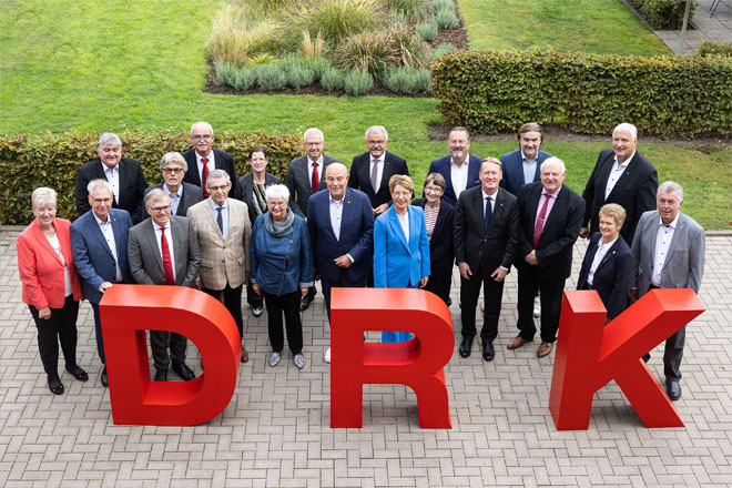 Die Präsidentinnen und Präsidenten der DRK-Landesverbände, des Verbandes der Schwesternschaften, Münsters Polizeipräsidentin sowie DRK-Präsidentin Gerda Hasselfeldt und Generalsekretär Christian Reuter stehen hinter großen roten Buchstaben "D", "R" und "K".