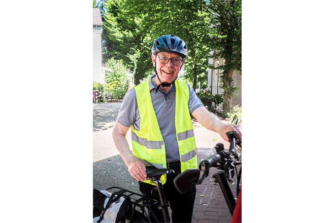 Mann mit Fahrradhelm und Warnweste steht neben einer Fahrradrikscha.