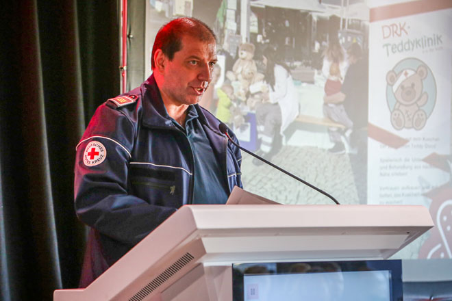 Ein Mann mit Jacke des Deutschen Roten Kreuzes steht an einem Rednerpult.