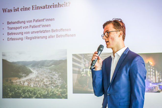 Ein junger Mann mit Mikrofon steht vor einer Präsentation.