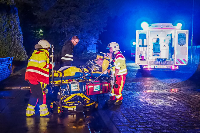 Zwei Sanitäter fahren einen Verletzten auf einer rollenden Trage zu einem Rettungswagen.