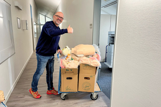 Ein Mann schiebt einen Wagen mit Umzugskartons in einen Raum und zeigt "Daumen hoch".